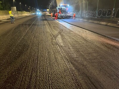 Hot mix asphalt wearing course being installed over the asphalt reinforcement grid